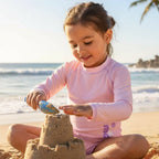 Child with long sleeve rash guard with marckids logo building a sandcastle on a beach with palm trees in the background
